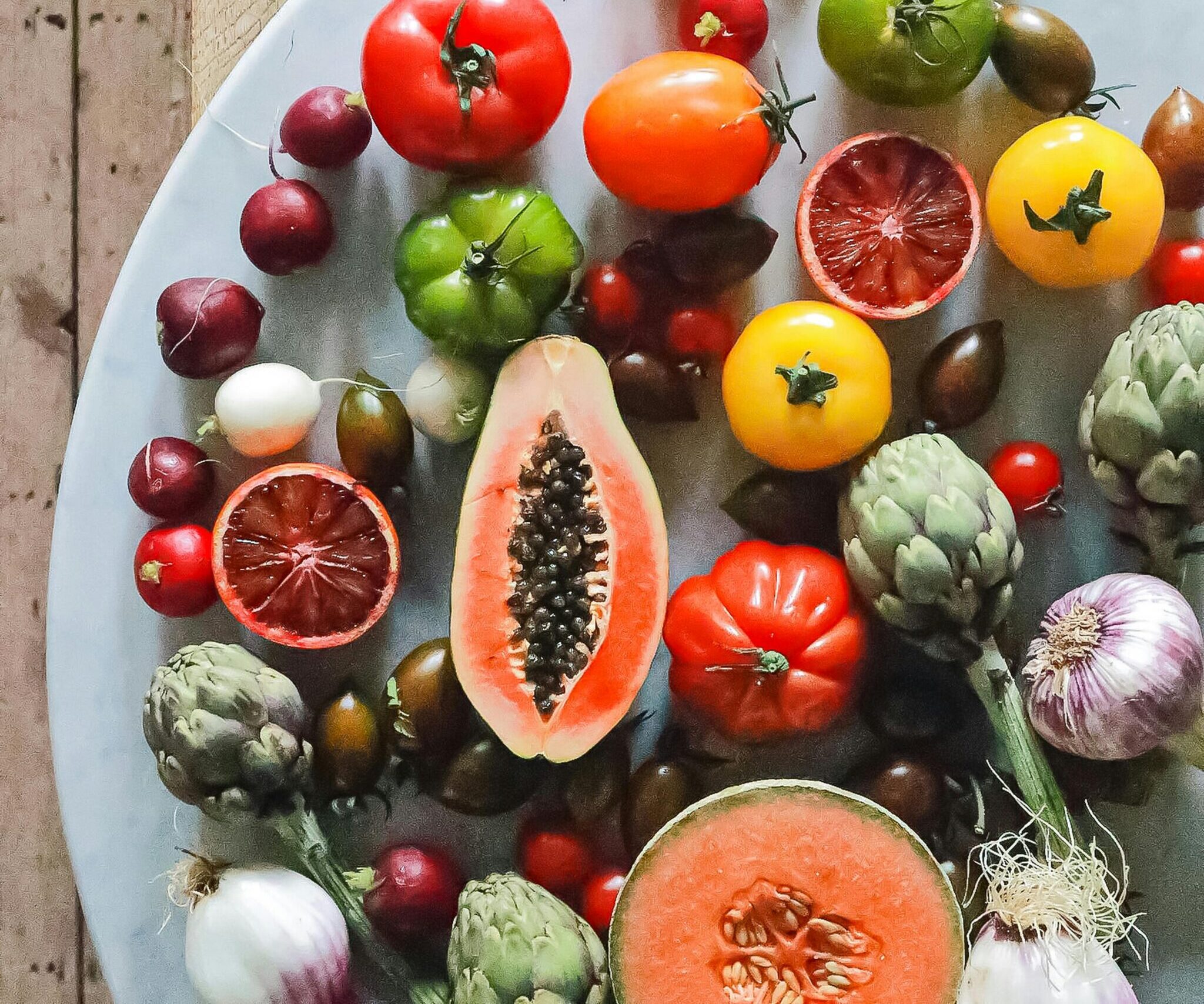 Top view of assorted exotic fruit with citrus and various vegetables of tomatoes and onions on round table
